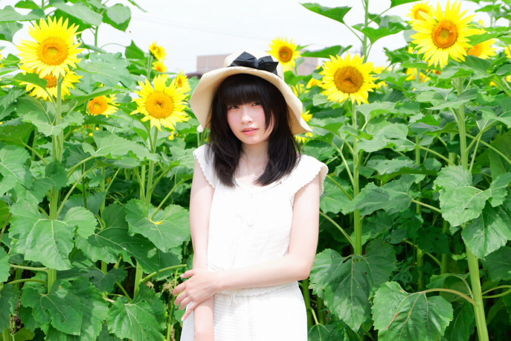 50mm標準画角:ひまわりを背景に自然な距離感で佇む女性モデルのポートレート