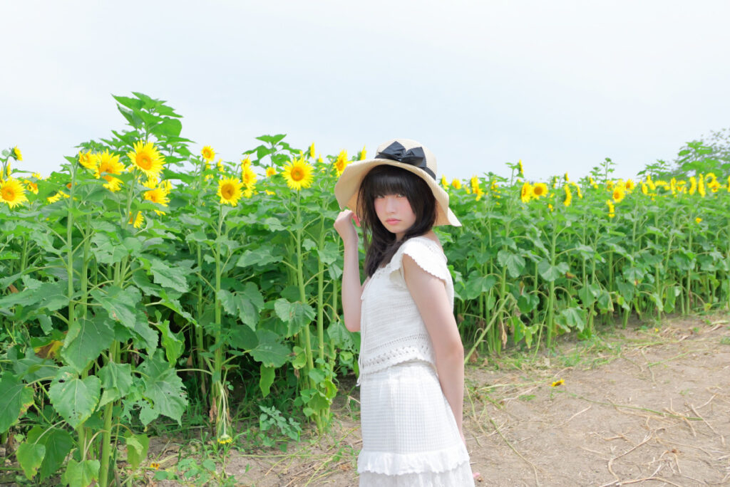 35mm画角:ひまわり畑の道中で優しく微笑む女性モデルのポートレート