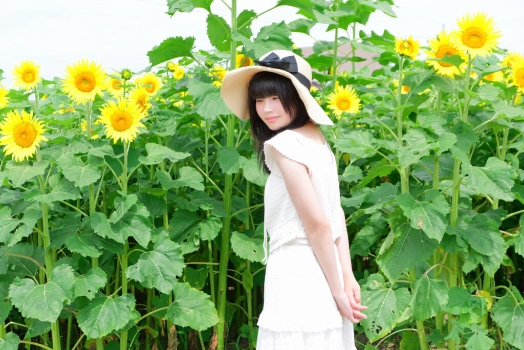 50mm標準画角:ひまわりに囲まれて少し俯く女性モデルのポートレート