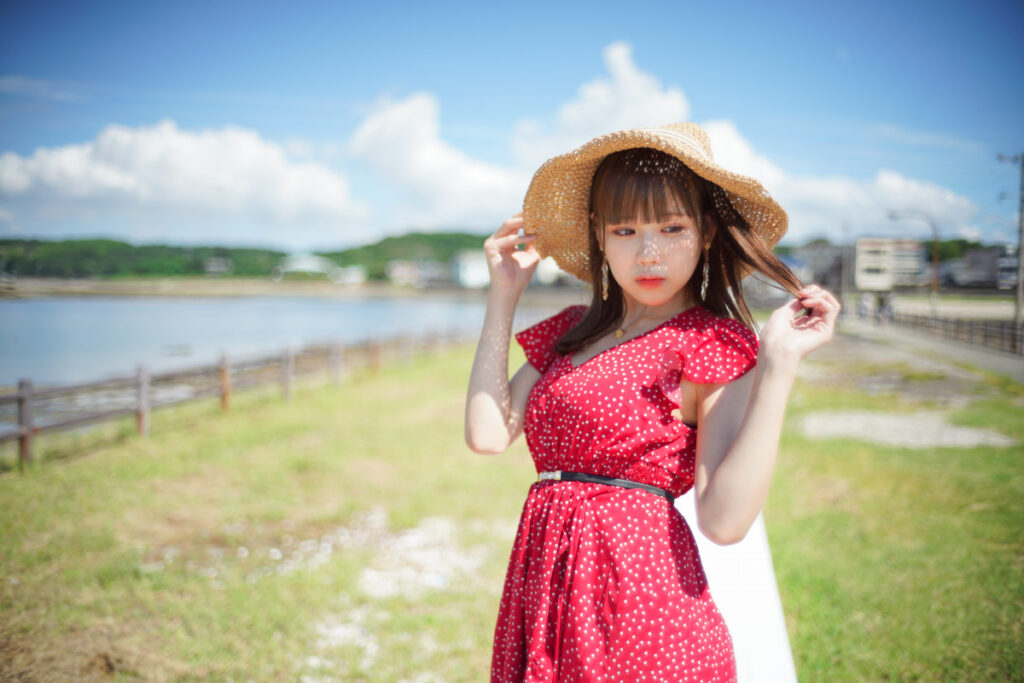 麦わら帽子の隙間から木漏れ日が差し込む、髪に手を添えた鹿乃ばんびさんのポートレート