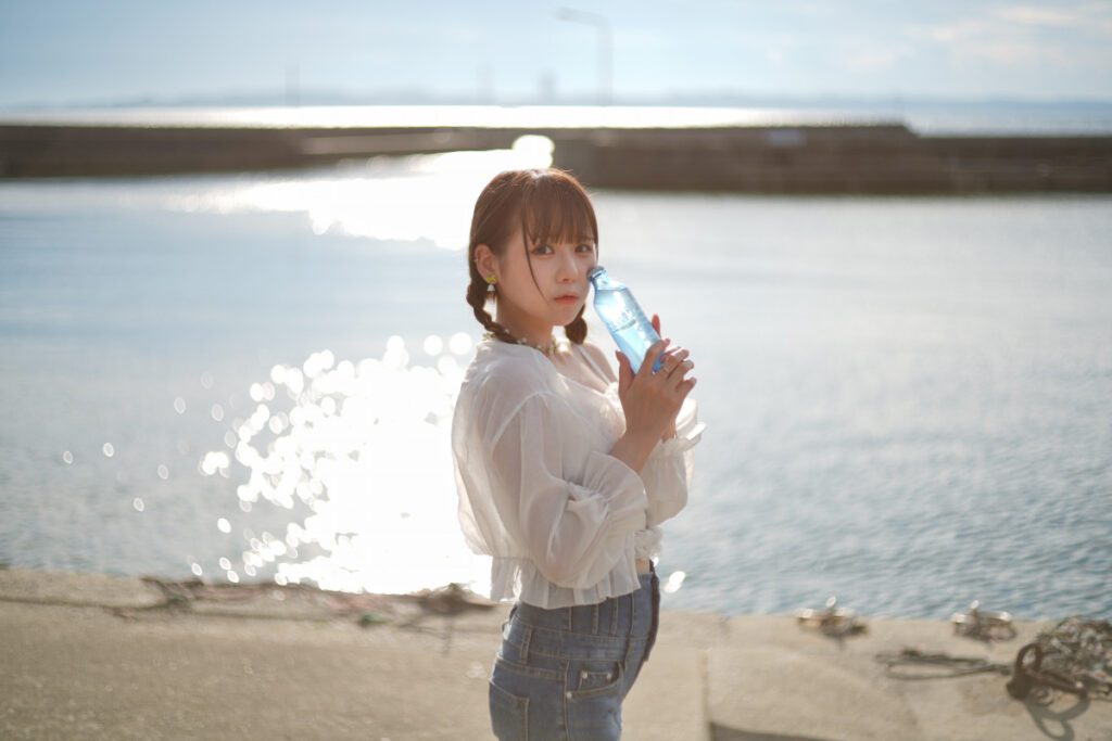 青いボトルを頬に当て、少しはにかんだような表情を見せる鹿乃ばんびさんのポートレート