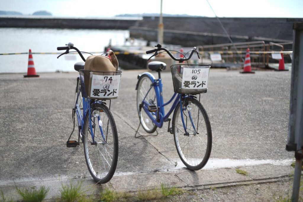 港の近くに2台並んで停められた青いレンタル自転車「愛ランド」のボケ味を活かしたカット