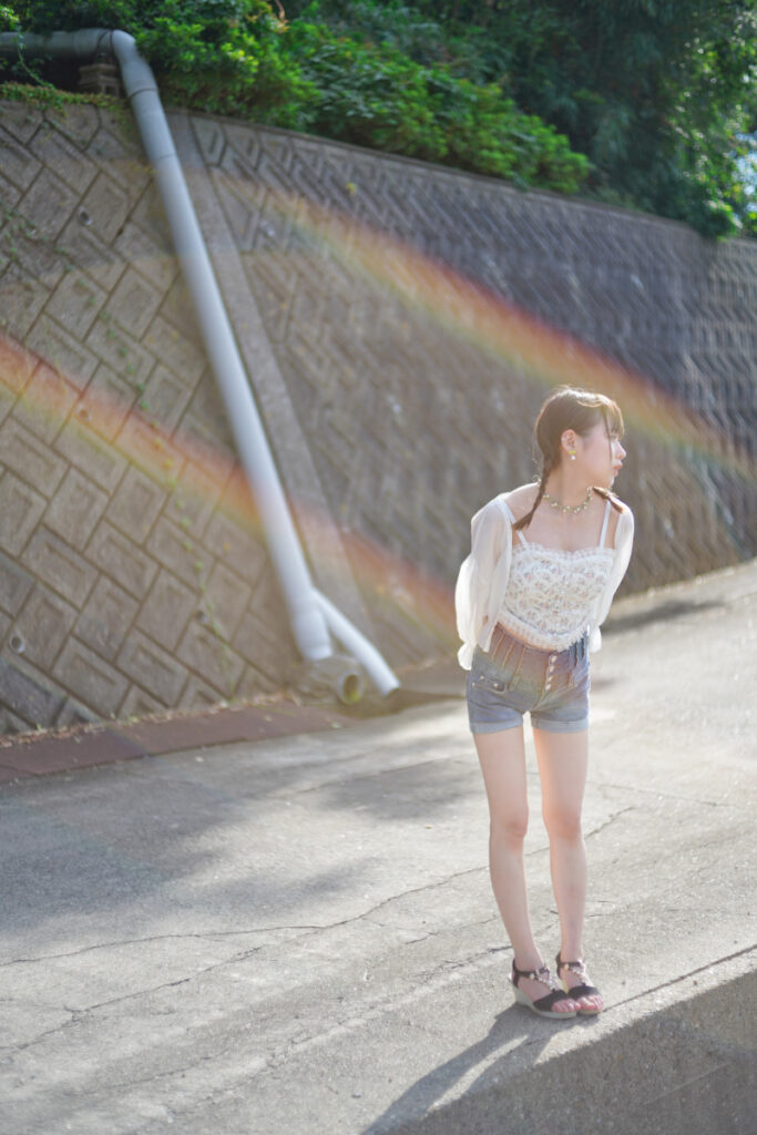 強い太陽光によって美しいレインボーフレアが出現した、コンクリート沿いに立つ鹿乃ばんびさんのポートレート