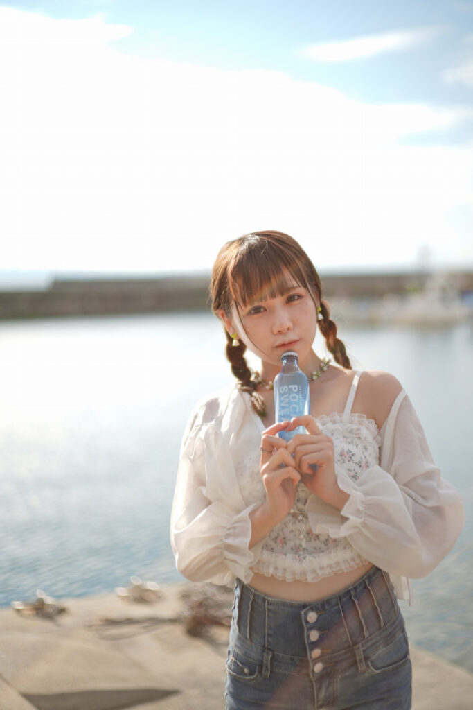 夏の強い逆光の中で、青いボトルを口元に当ててカメラを見つめる鹿乃ばんびさんのポートレート