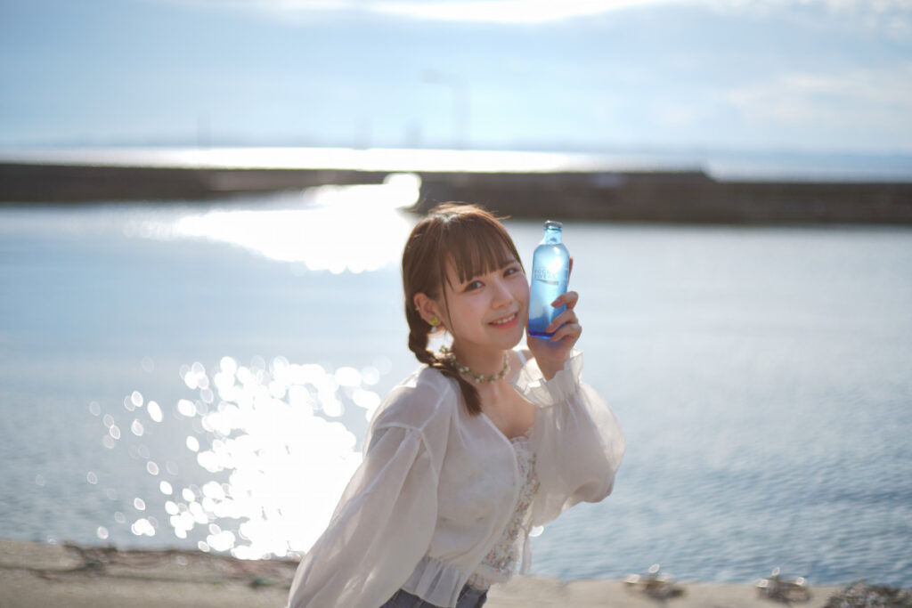 眩しい海の玉ボケに包まれながら、カメラに向かって弾けるような笑顔を見せる鹿乃ばんびさん