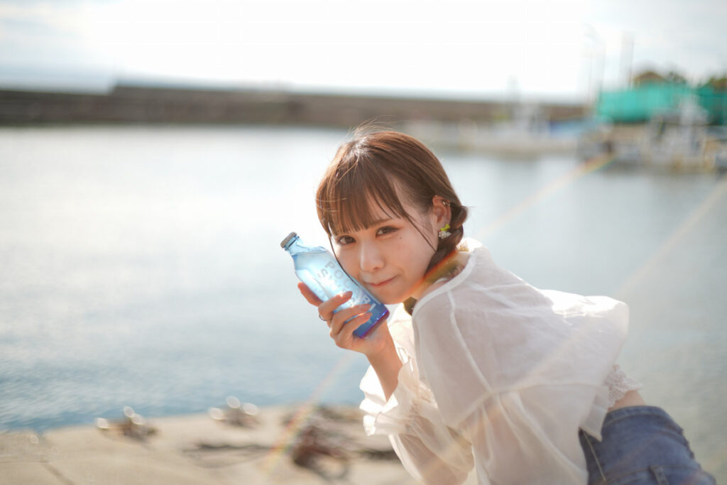 海の眩しい玉ボケと虹色の光に包まれながら、優しい笑顔を覗かせる鹿乃ばんびさん