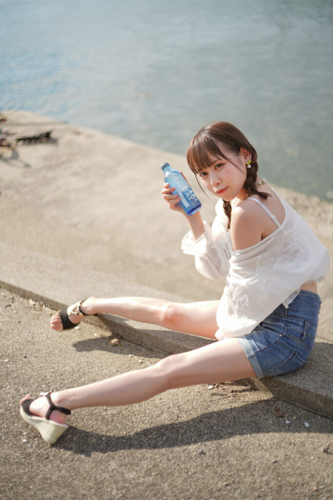 堤防の上に腰掛け、足を伸ばしてリラックスした表情を見せる鹿乃ばんびさんの座りシーン