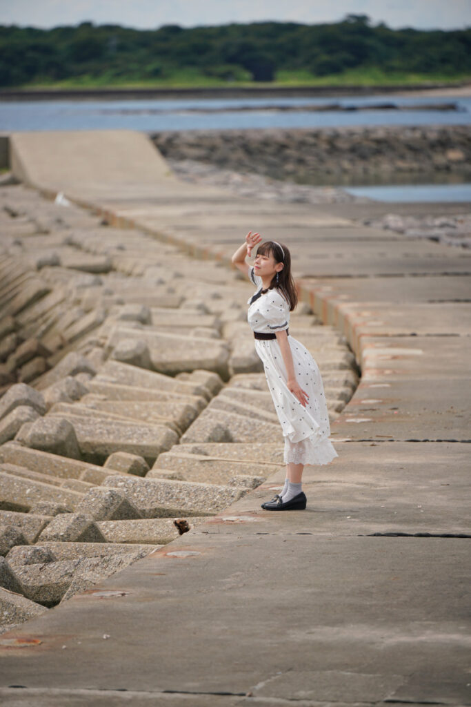 佐久島の海岸沿いにある長い堤防の上に立ち、海を見つめる鹿乃ばんびさんの望遠ポートレート