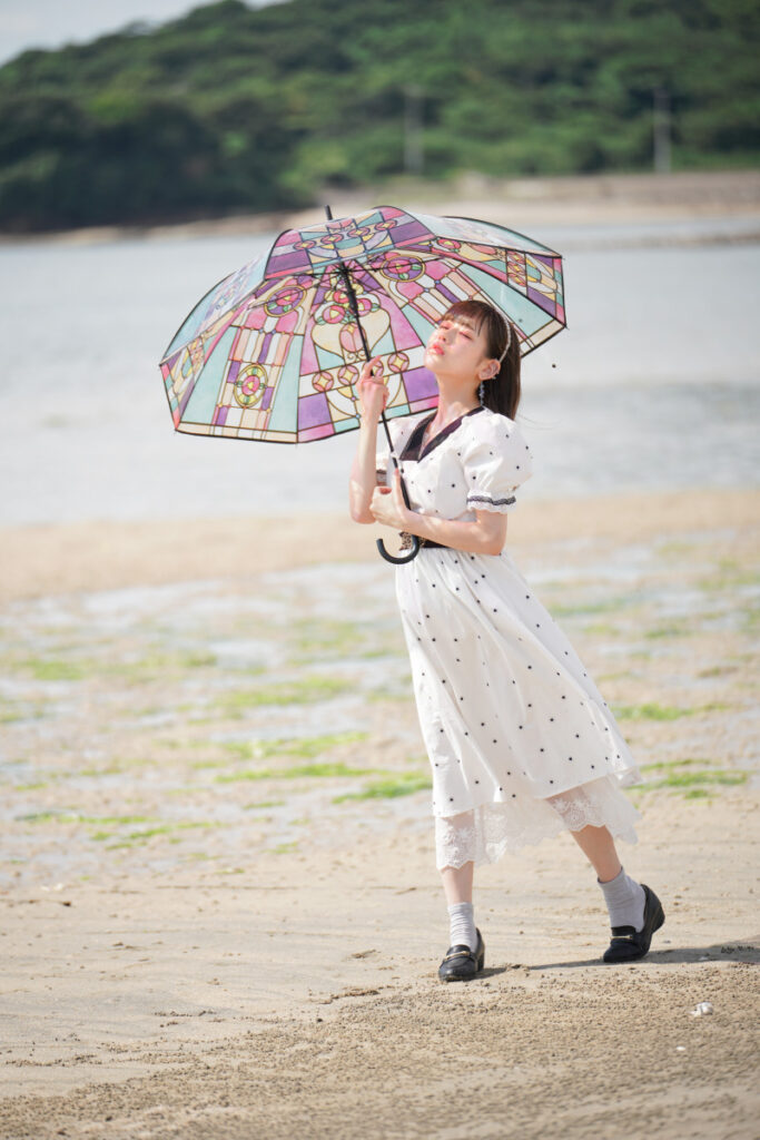 海岸の砂浜でステンドグラス傘を差し、そっと目を閉じて夏の風を感じる鹿乃ばんびさん
