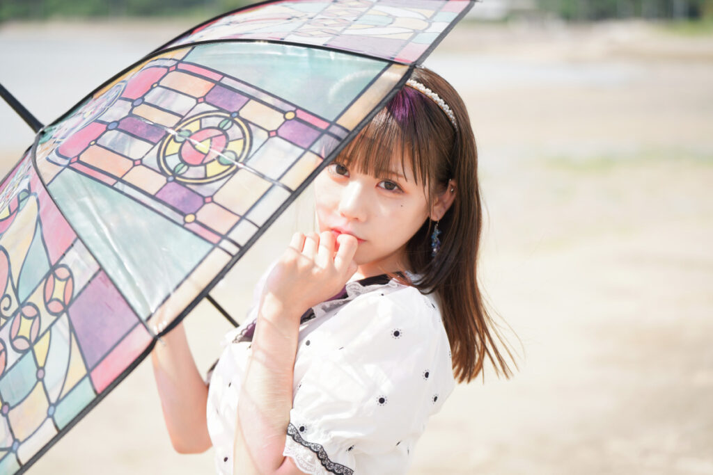 傘を透過した鮮やかな色彩の光が顔に美しく映り込む、口元に手を添えた鹿乃ばんびさんのクローズアップ