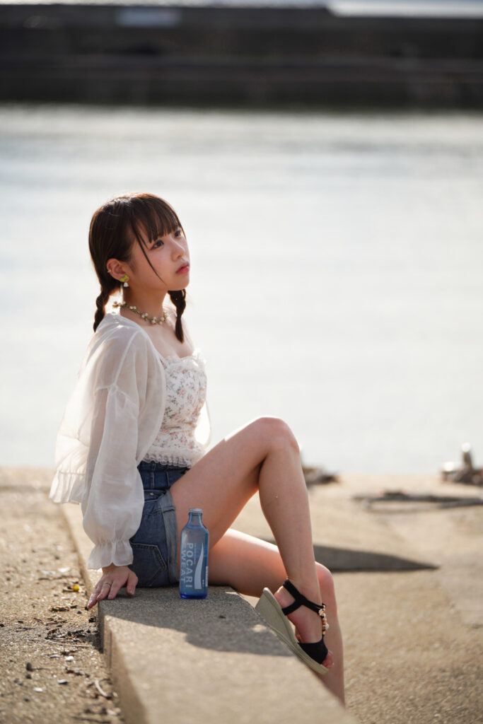 海からの逆光を浴びながら、堤防の上に腰掛けて遠くを見つめる鹿乃ばんびさんの美しい佇まい