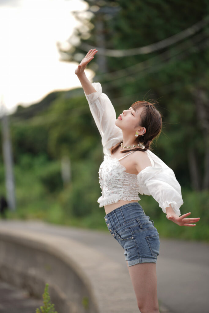 黄昏時の心地よい風を受け、目を閉じて両手を広げる鹿乃ばんびさんのサイドビュー