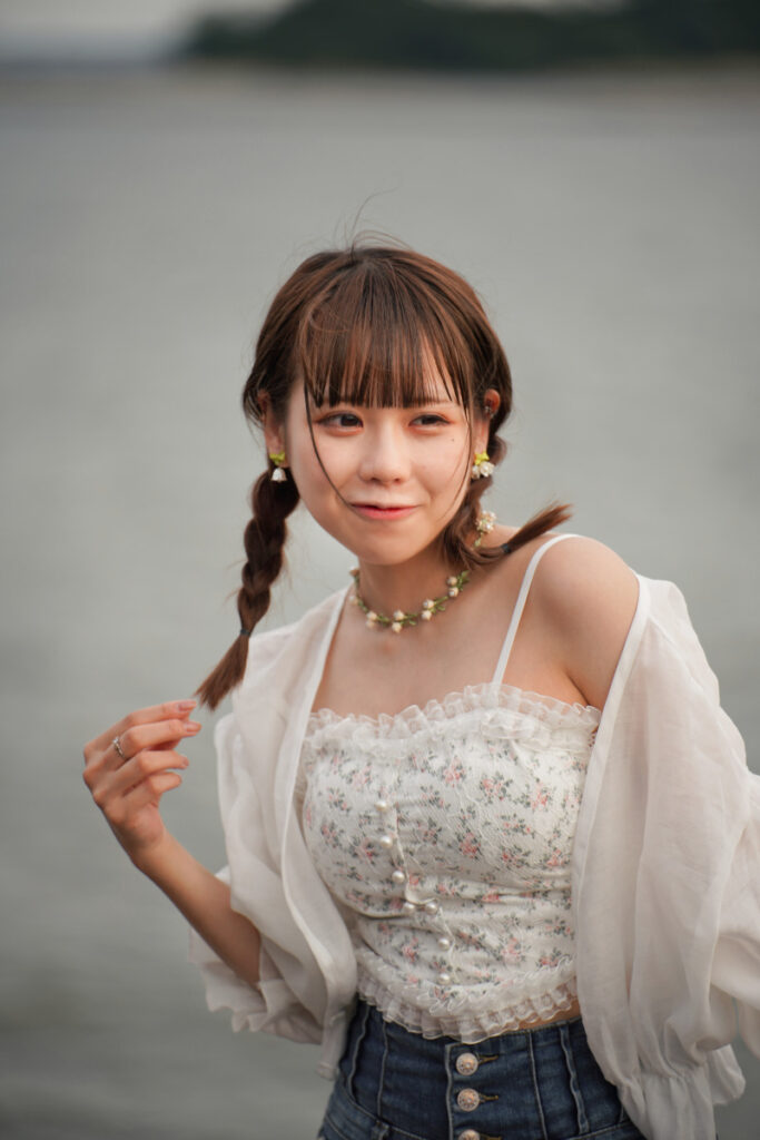 三つ編みにした髪の毛の先を指で持ち、優しく微笑む鹿乃ばんびさんの夕暮れクローズアップ
