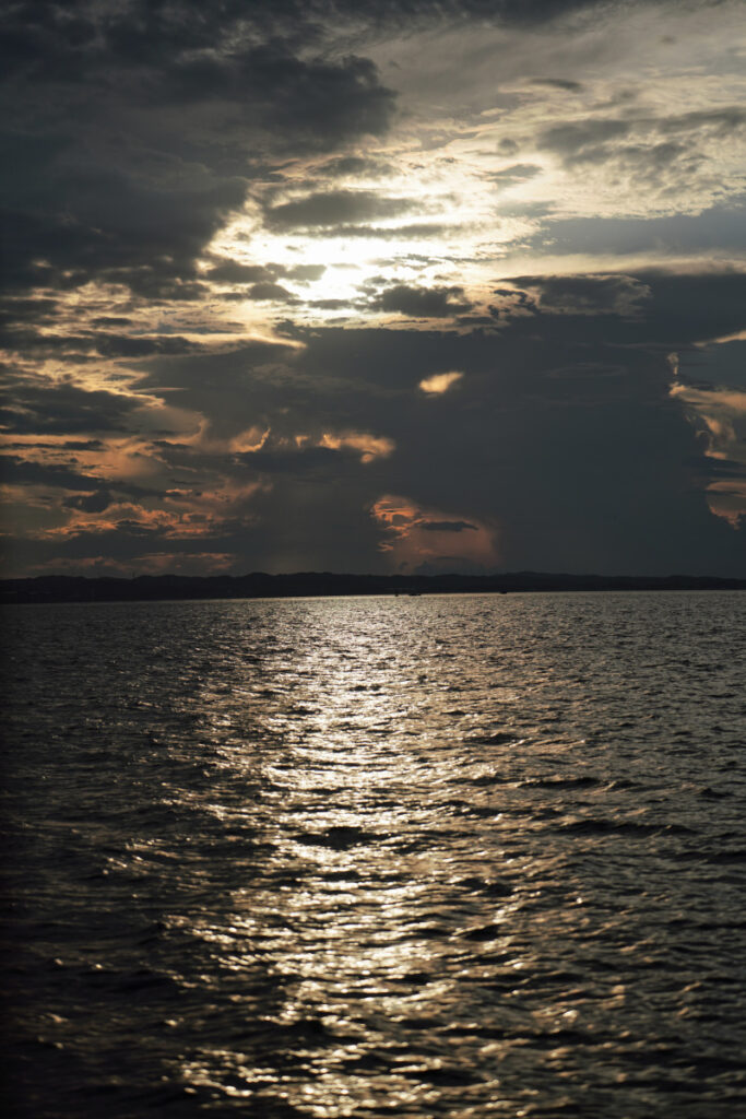沈みゆく夕日の光が水面にキラキラと一筋に反射する、佐久島の静かな海の風景