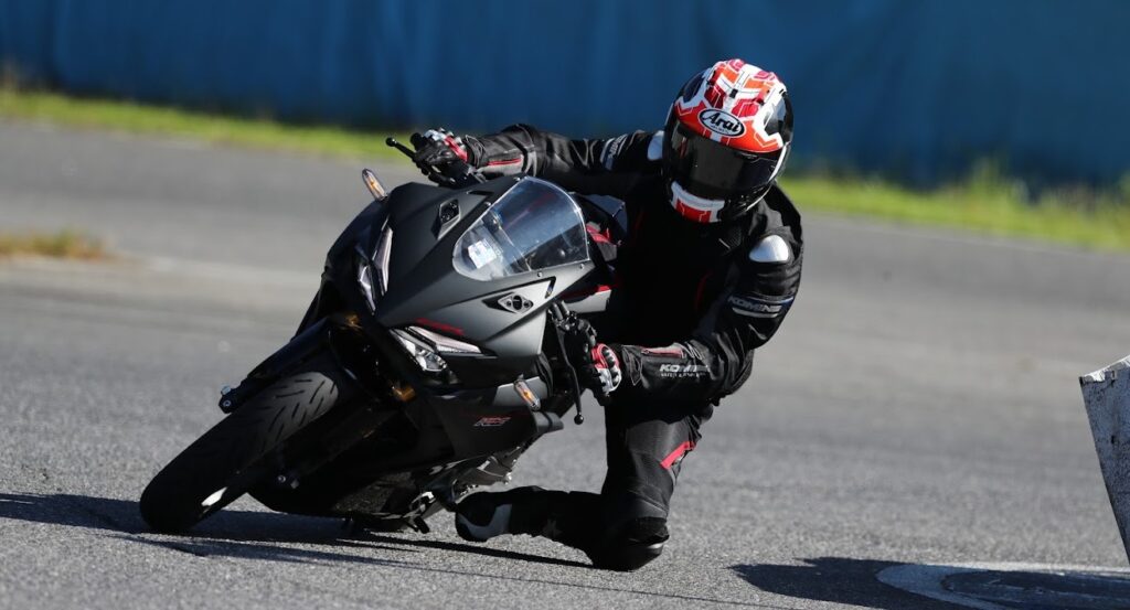 サーキットで膝を擦りながらハングオンでコーナリングするマットブラックのCBR250RRとライダーの写真