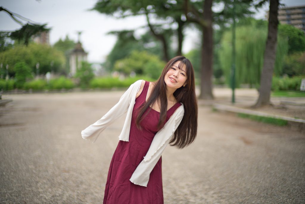 首をかしげて微笑む桜井こはるさんと背景の噴水塔(開放F1.0)