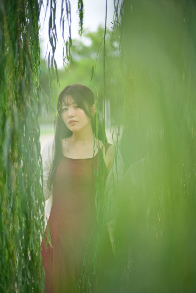 柳の葉越しにこちらを見つめる桜井こはるさんの幻想的な作例(開放F1.0)