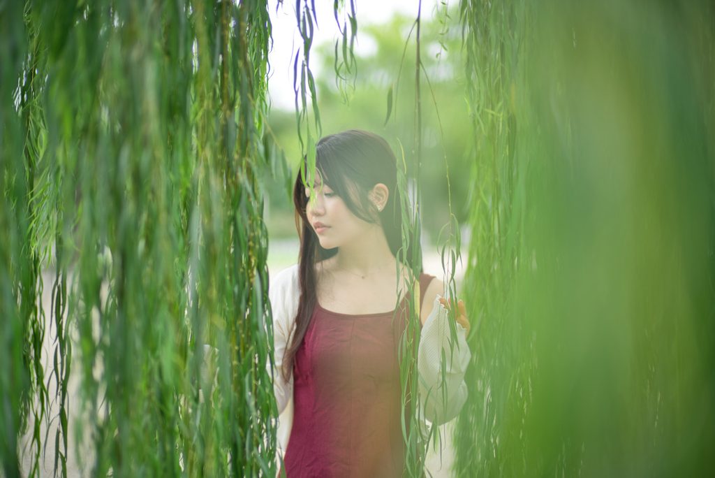 柔らかな緑の前ボケと光の滲みに包まれる桜井こはるさんの横顔(開放F1.0)