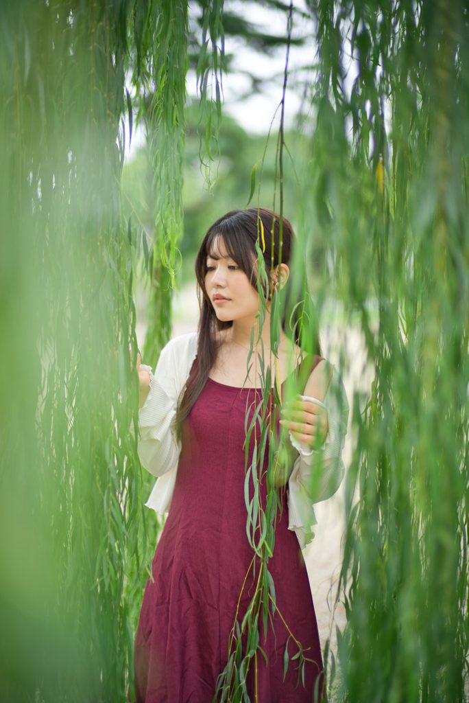 枝垂れ柳の前ボケに包まれる桜井こはるさんのウエストアップポートレート(開放F1.0)