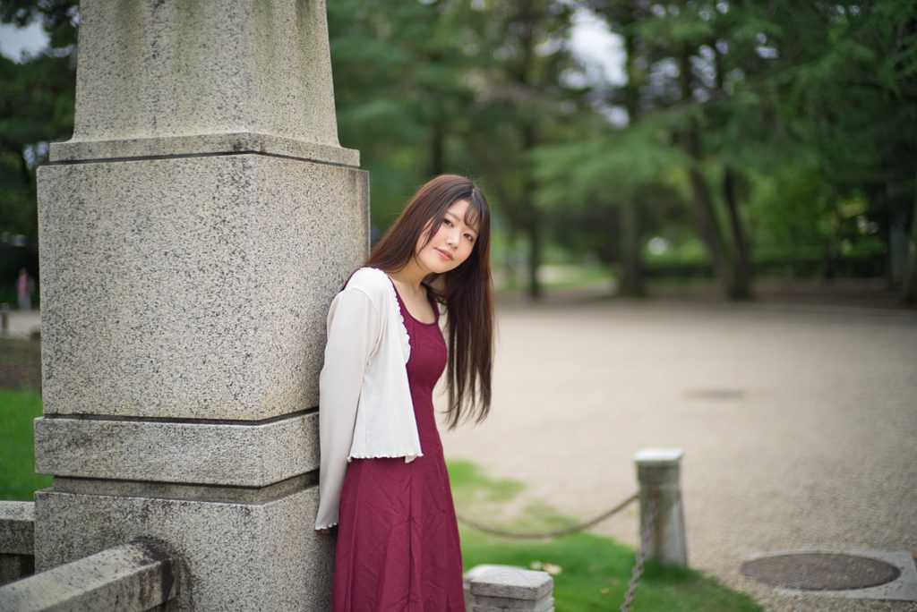 鋳鉄金具のある石柱に寄り添い遠くを見つめる桜井こはるさん(開放F1.0)