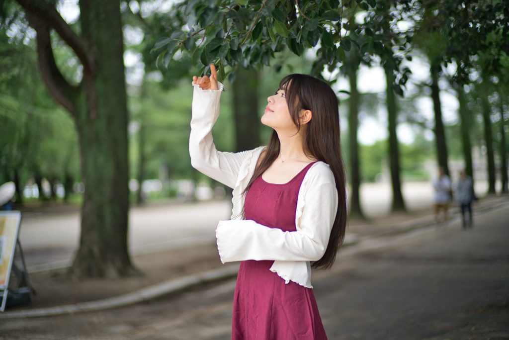 垂れ下がる木の葉に手を伸ばす桜井こはるさんのポートレート(開放F1.0)