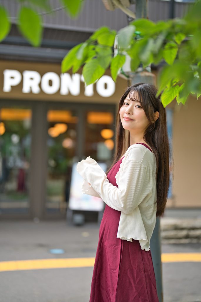 木葉の前ボケとPRONTOの看板を背景に捉えた開放F1.2の縦構図ポートレート
