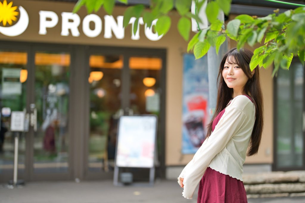 木葉の前ボケとPRONTOの看板を背景に捉えた開放F1.2の縦構図ポートレートの横構図